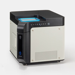 Compact benchtop laboratory instrument with a blue-lit interior and beige panels viewed from the front-left.